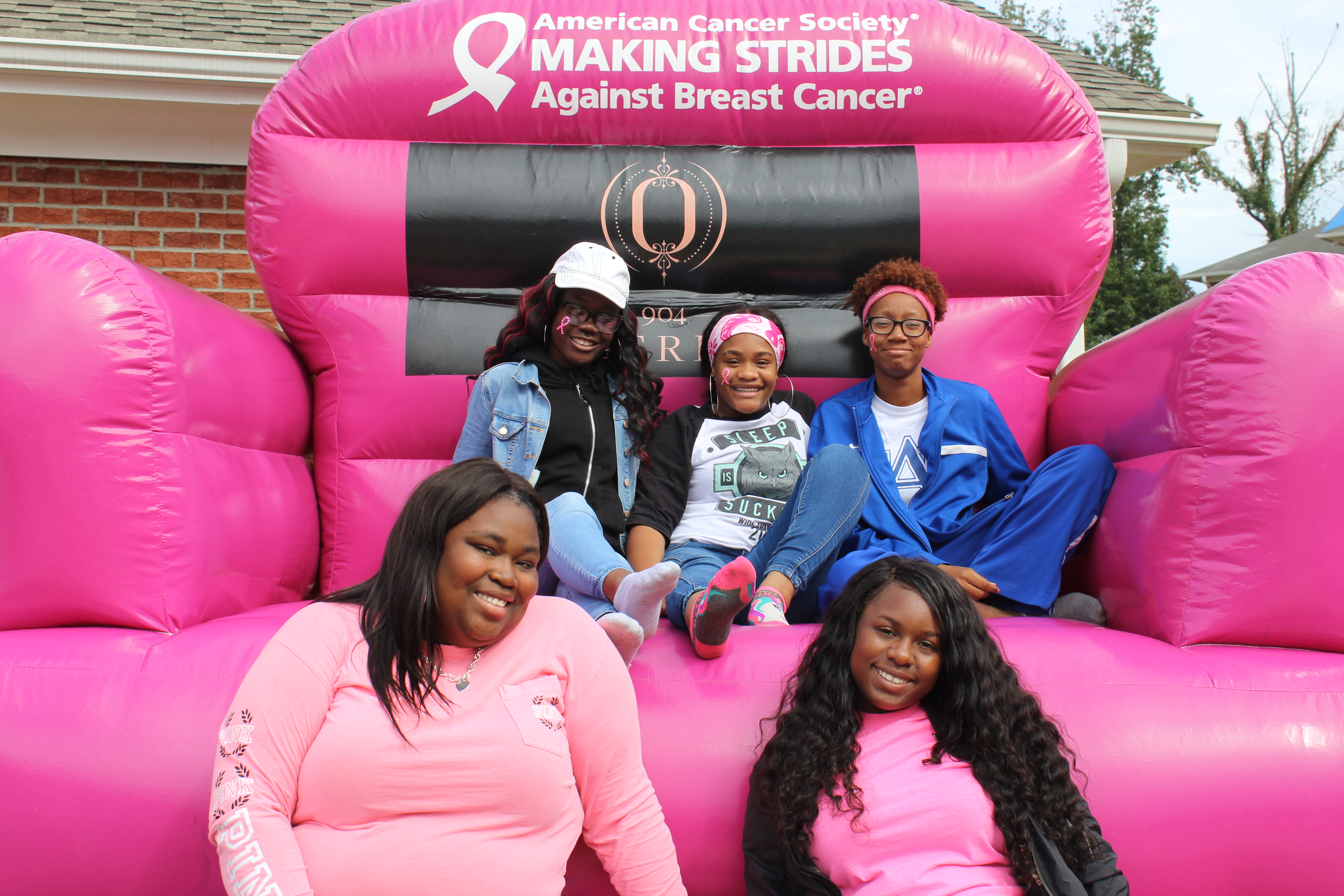 Five girls posed in front of giant, inflatable, pink chair. In honor of Breast Cancer Awareness