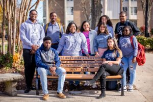 group of students sitting on and standing around a bench on campus