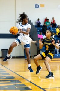 Female SAU Basketball player jumping while catching basketball and defending against opponent